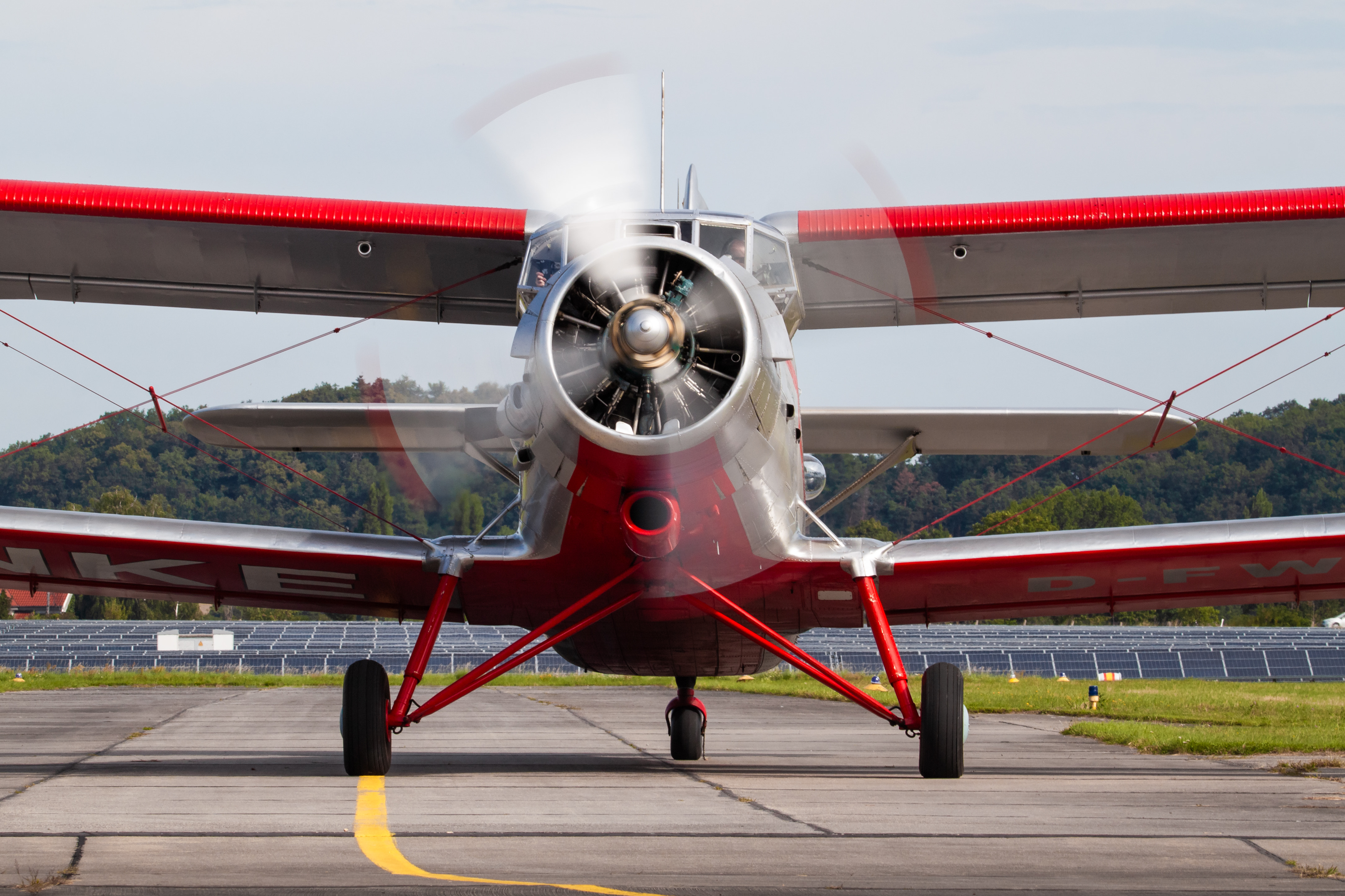 Rundflugtage & Pianoabend – Flugplatz Taucha 03./04.10. Frontalansicht eines Doppeldeckers mit rot-weißen Akzenten auf dem Rollfeld eines Flugplatzes, umgeben von grüner Landschaft.