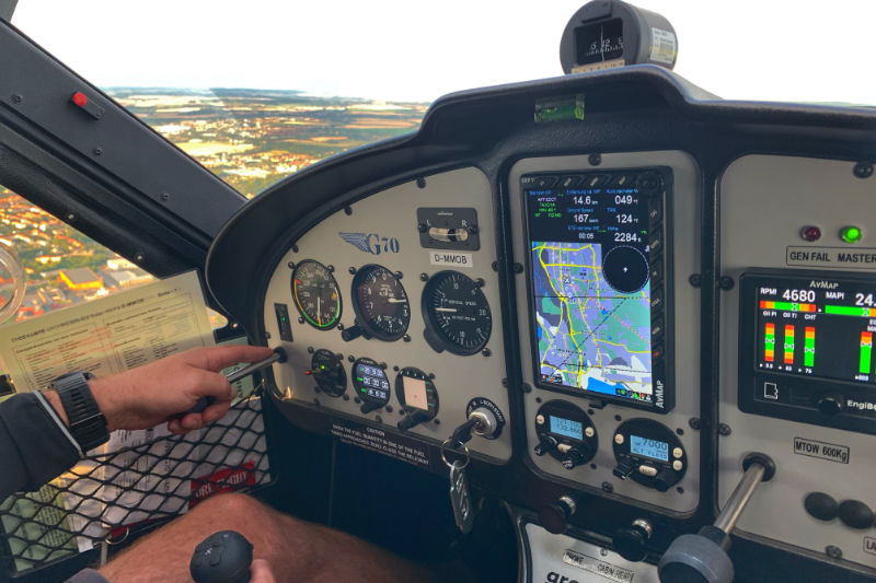 Nahaufnahme des Cockpits eines einmotorigen Flugzeugs mit einem Piloten, der auf die Instrumententafel zeigt, während eine Karte auf dem Navigationsbildschirm angezeigt wird