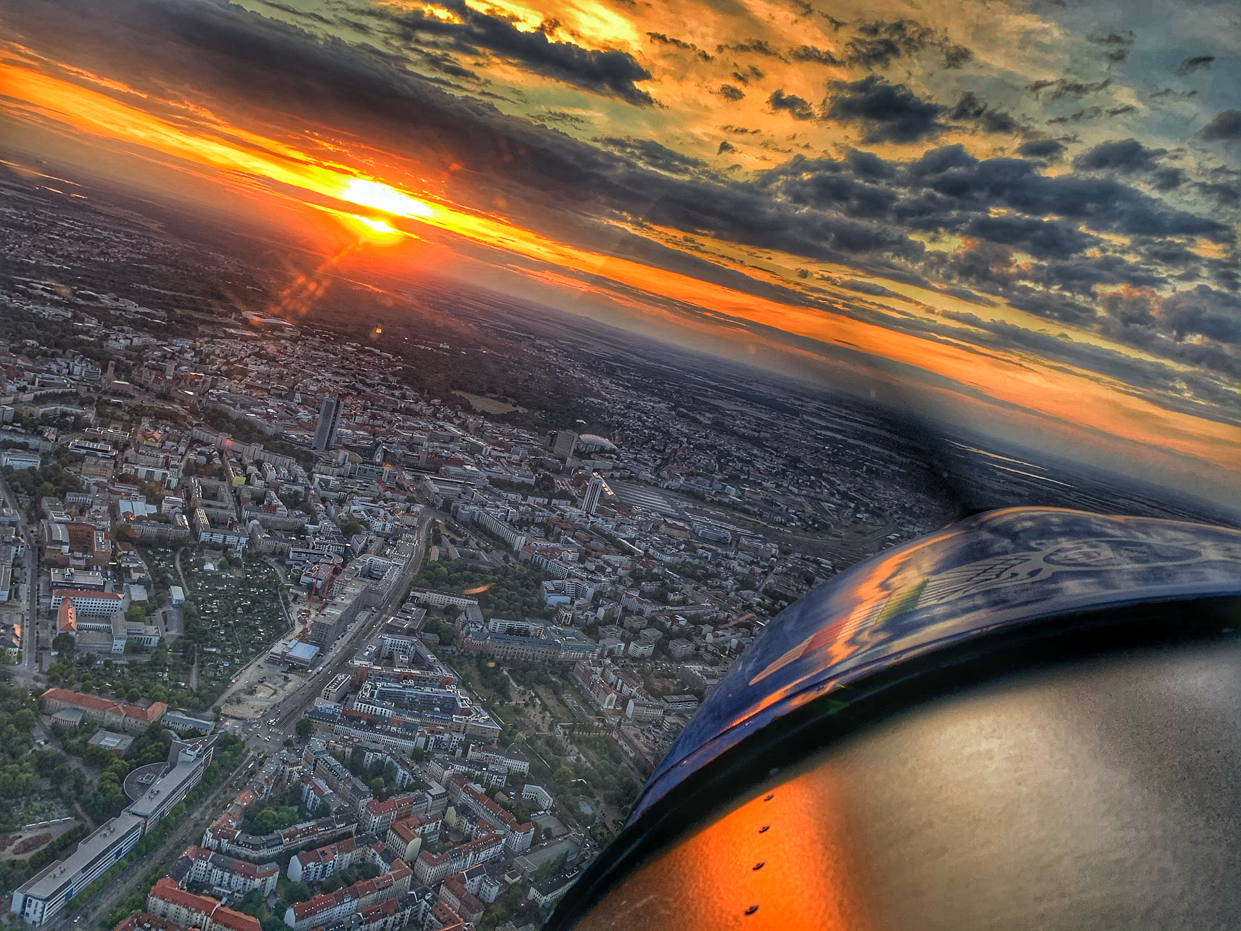 Blick aus einem Flugzeug auf eine Stadtlandschaft bei Sonnenuntergang mit Wolken am Himmel