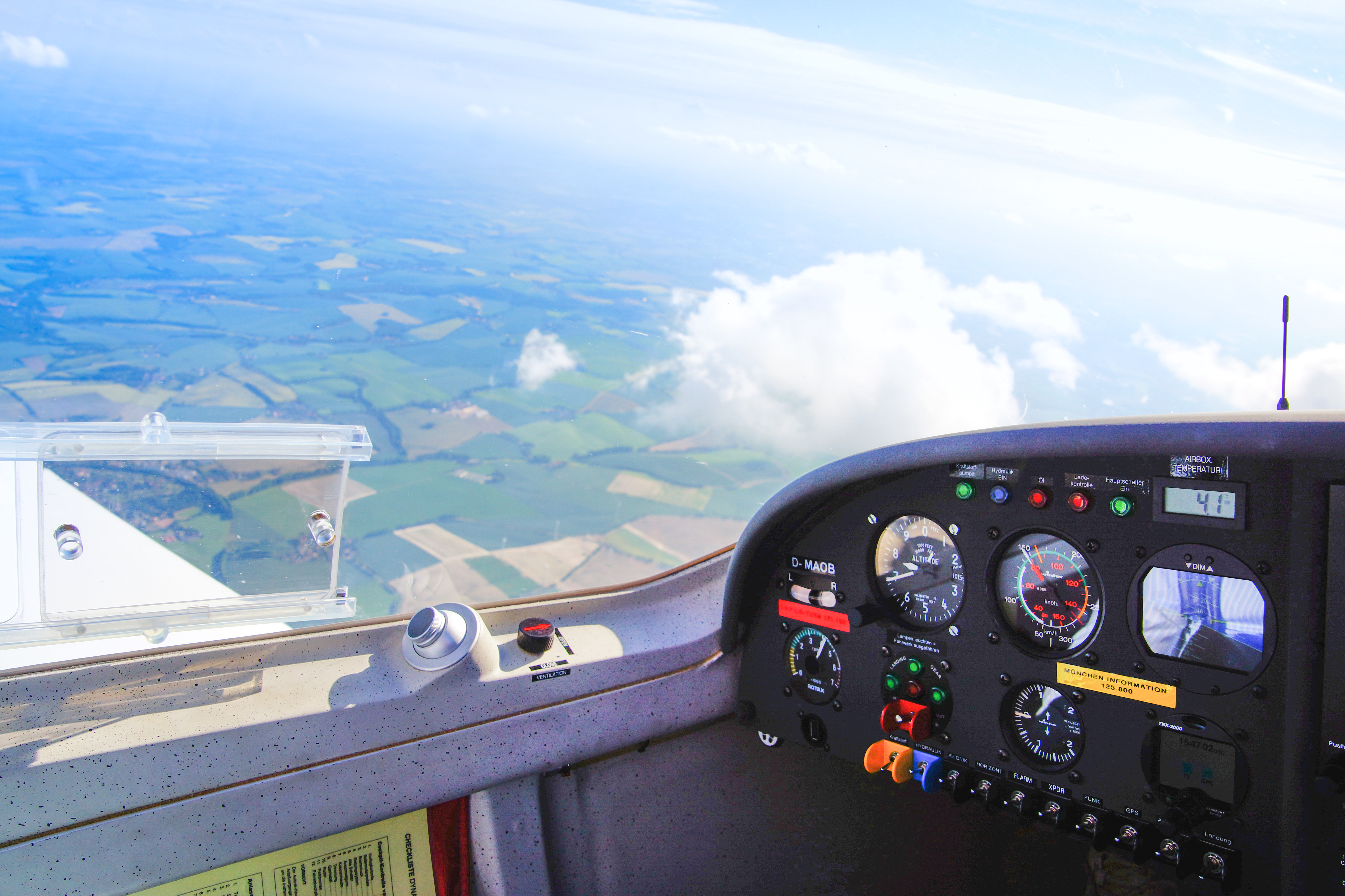 Blick aus dem Cockpit eines Leichtflugzeugs auf das Armaturenbrett und die darunter liegende Weizenfelderlandschaft