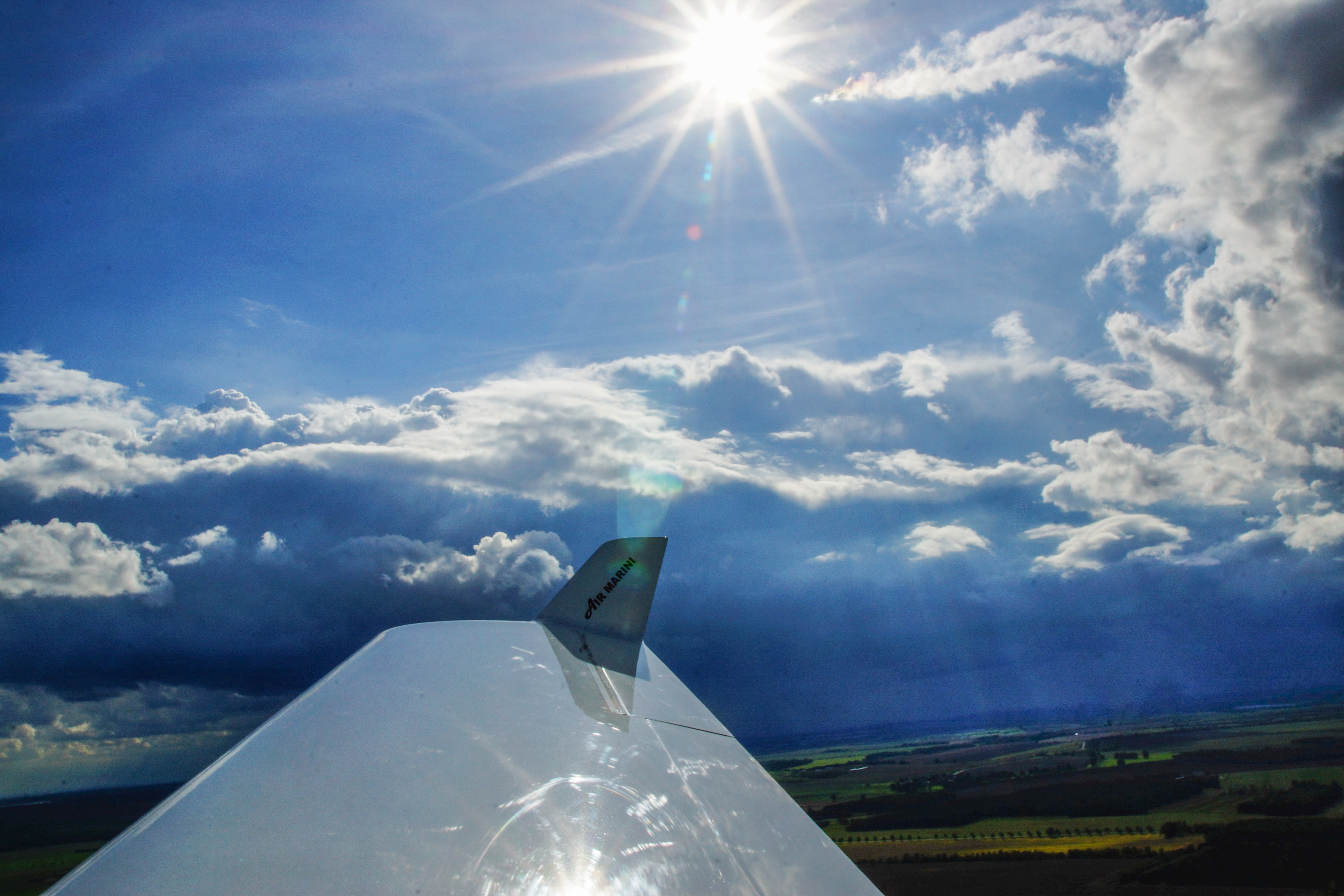 Blick von einem Flugzeugflügel über eine Landschaft mit Wolken und Sonnenschein