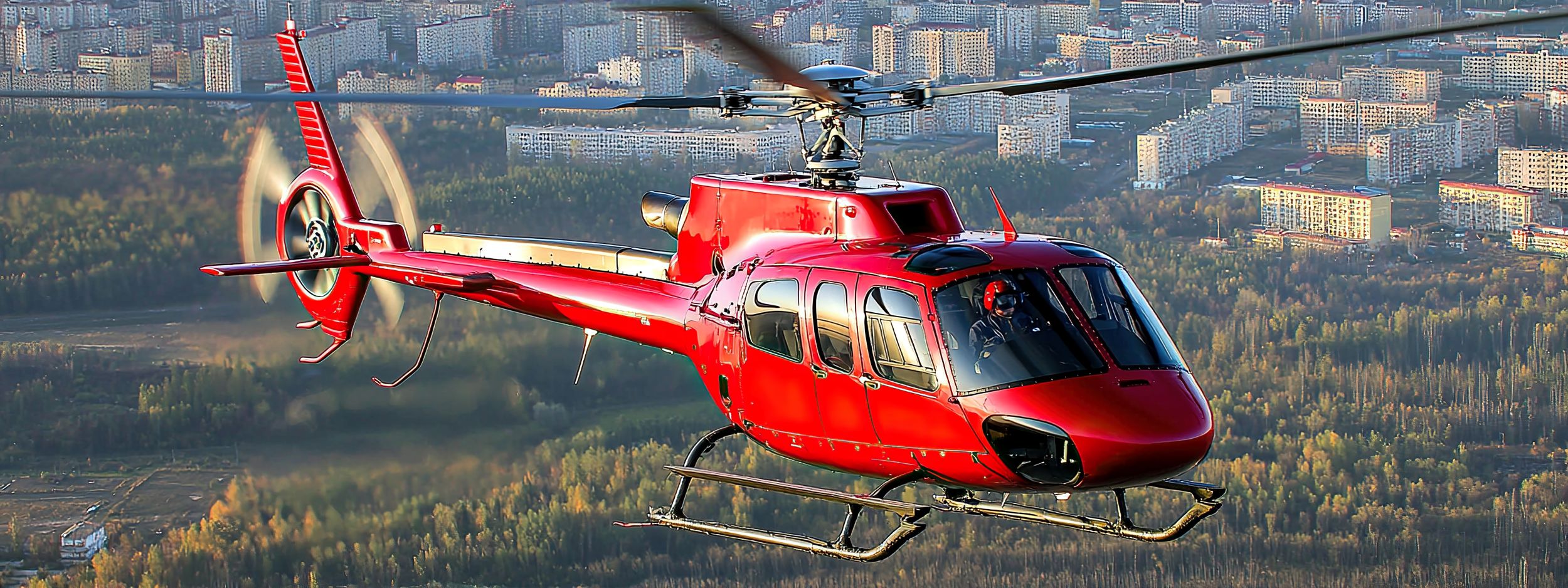 Ein roter Hubschrauber fliegt über eine städtische Landschaft mit Hochhäusern und Bäumen im Hintergrund.