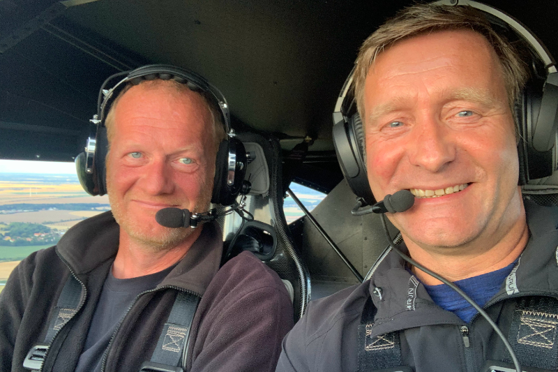 Pilot für einen Tag Zwei Männer mit Headsets lächeln in die Kamera, während sie im Cockpit eines Flugzeugs sitzen